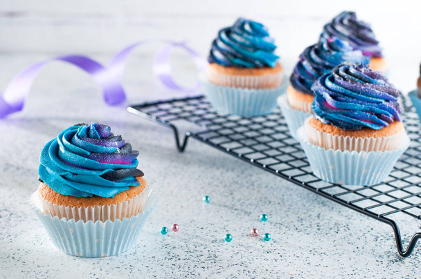 Vanille-Cupcakes mit Galaxie-dunkler Schlagsahne auf hellem Hintergrund. Selektiver Fokus. - Foto, Bild