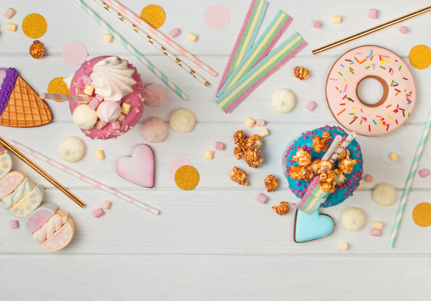 Happy Birthday Party Hintergrund mit zwei Freak Shakes, Donut, Marshmallow, Baiser, Popcorn und Marmelade auf weißem Holzhintergrund mit Leerraum für Text; Draufsicht, flache Lage - Foto, Bild