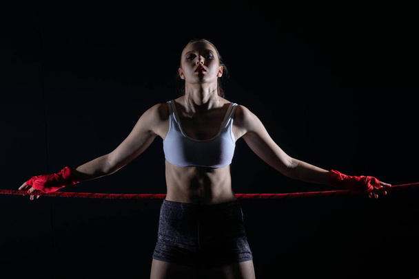 Urheilija perustuu nyrkkeilykehän punaiseen köyteen. Päättäväinen nainen seisoo kehässä valmiina aloittamaan taistelun. - Valokuva, kuva