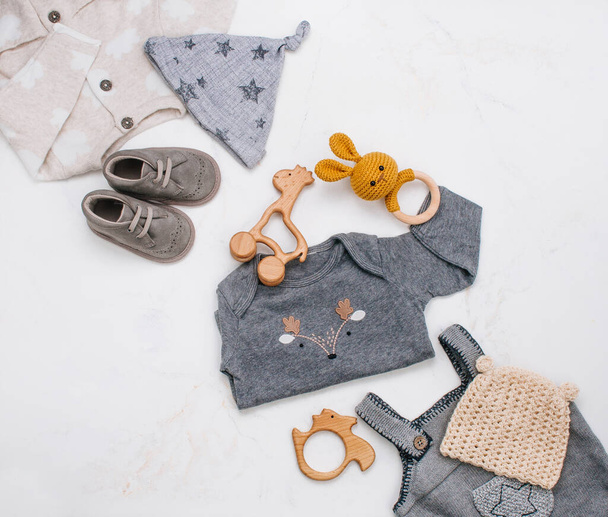 新生児の服、木製のビーンズバッグ、歯とおもちゃは、テキスト用の空白のスペースで明るい大理石の背景にあります。トップビュー、フラットレイアウト. - 写真・画像