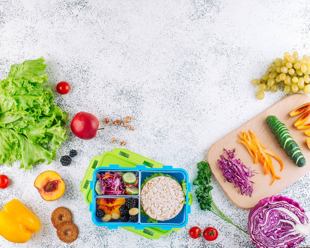 Открытая обеденная коробка с бутербродами, хрустящим хлебом, фруктами и овощами с ингредиентами
 - Фото, изображение