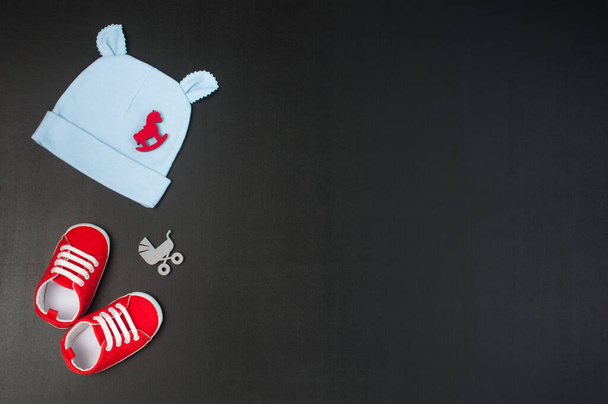 Kırmızı bebek ayakkabıları, şapka ve bebek aksesuarları siyah tebeşir tahtası arka planında mesaj için boş alan. Üst manzara, düz uzanma. - Fotoğraf, Görsel