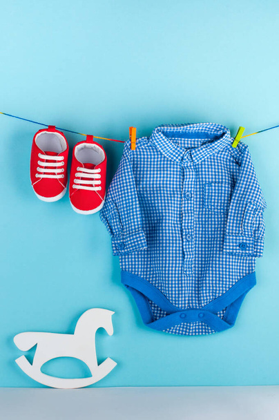 Red baby booties and blue body kit on clothespins over blue background with blank space for text. - 写真・画像