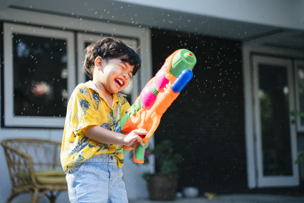 Little boy splash the water with water gun and rubber tube at his house in Songkran day, the yearly traditional day of Thailand. - Foto, imagen