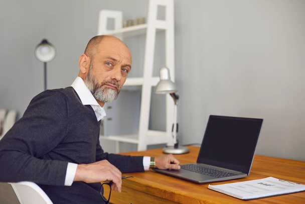 Online job concept. Serious elderly man working or studying at home on his laptop computer, mockup for design - Foto, Imagem