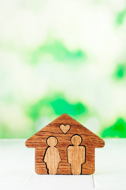Οικογενειακό σπίτι. Ξύλινο σπίτι με φιγούρες του άνδρα και της γυναίκας μέσα σε λευκό φόντο με κενό χώρο για κείμενο. - Φωτογραφία, εικόνα