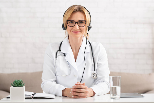 Consultation with specialist. Female doctor with headphones looks at camera - Foto, imagen