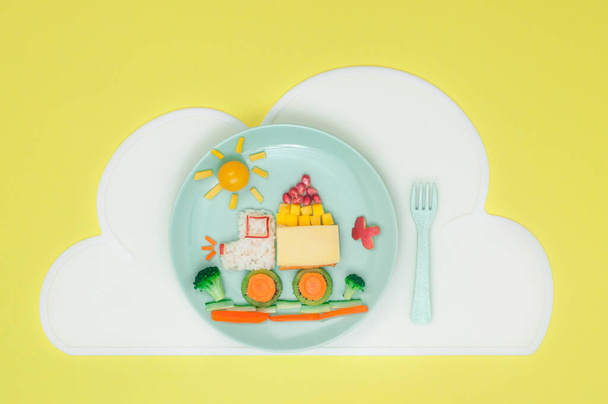 Kids food art concept: auto van rijst, sandwich en verse groenten en fruit op de plaat met wolkenservet op de gele achtergrond met lege ruimte voor tekst; bovenaanzicht, plat gelegd - Foto, afbeelding