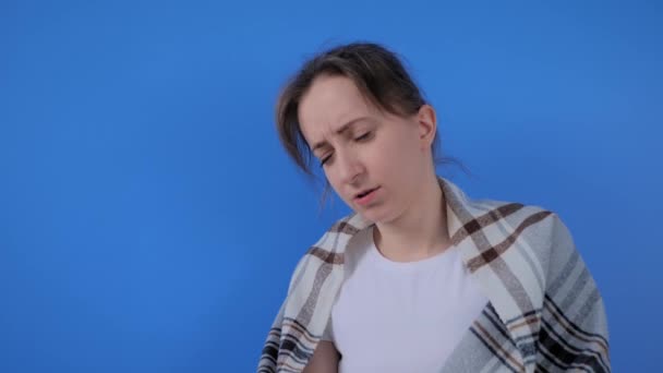 Slow motion: woman feeling sick, sneezing into facial tissue against blue wall - Footage, Video