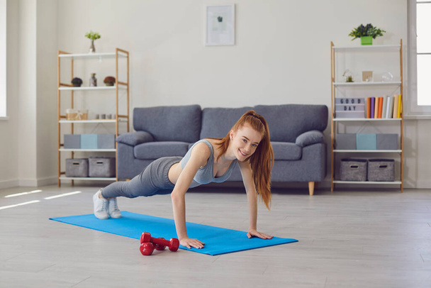 Home sports. Beautiful girl doing push ups or plank on yoga mat indoors. Fit young woman working out in living room - Photo, image