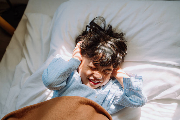 Little boy close his ears while the alarm clock ring to wake him up in the morning but he want more sleeping. - Foto, Imagen