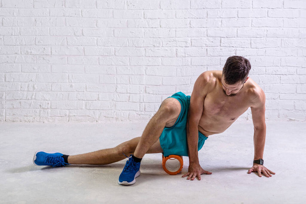 A young man in shorts does exercises on a roller from foam to his legs. Exercise on a foam roller. - Foto, imagen