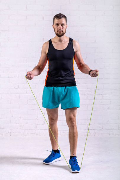 A young man holds a rope in his hands, standing near a white wall. Active lifestyle. - Foto, Imagen