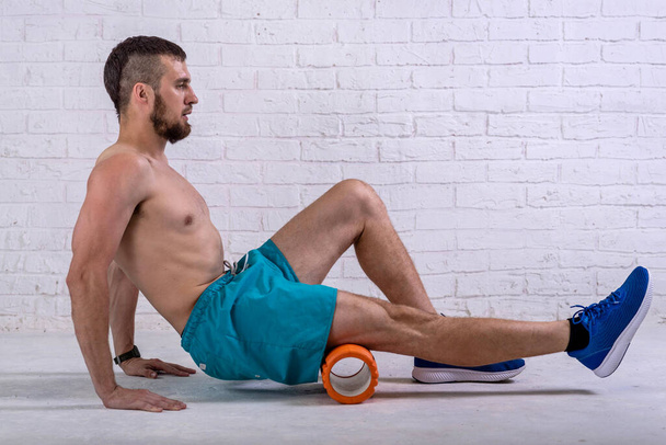 A young man in shorts does exercises on a roller from foam to his legs. Exercise on a foam roller. - Photo, Image
