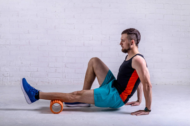 A young man in shorts does exercises on a roller from foam to his legs. Exercise on a foam roller. - Foto, imagen