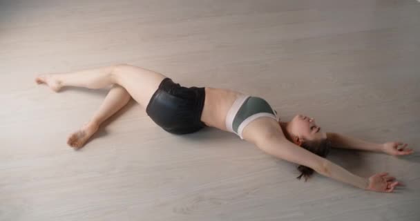 Aantrekkelijke jonge vrouw doet gymnastische oefeningen op de vloer en strekt zich uit, yoga lessen in slow motion, persoon maakt fysieke training, stretching en gymnastiek, 4k 120p Prores HQ 10 bit - Video