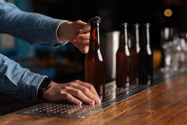 Bebidas en pub de moda. Barman abierto botellas de cerveza en barra de madera contador
 - Foto, Imagen