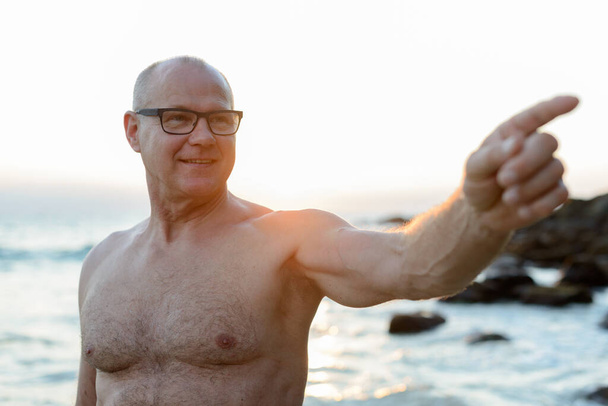 Portrét zralého pohledného turisty bez košile relaxaci na pláži venku - Fotografie, Obrázek