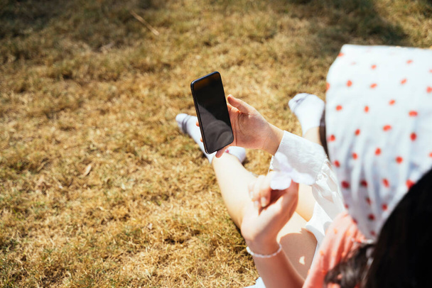 彼女は夏の日差しの中で座っている間、女性の手にスマートフォンの作物の画像. - 写真・画像