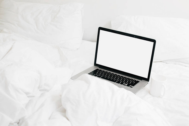 Stylish laptop with blank screen and coffee cup on white soft bed, copy space. Shopping or working online from home. Mockup. Freelance and freelancer. Staying home. Blog template - Foto, immagini