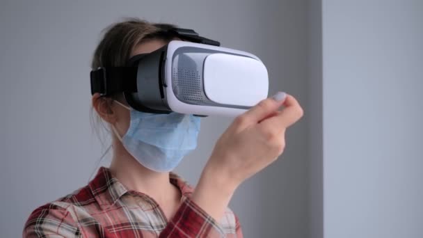 Młoda kobieta ubrana w medyczną maskę twarzy i zestaw słuchawkowy wirtualnej rzeczywistości - koncepcja VR - Materiał filmowy, wideo