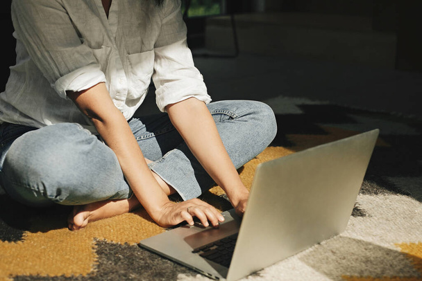 Menina elegante hipster usando laptop, sentado no tapete chão no quarto moderno em luz ensolarada. Jovem mulher fazendo compras ou trabalhando online a partir de casa. Freelance e freelancer
 - Foto, Imagem