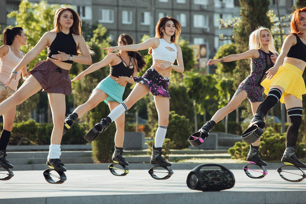 Beautiful women in sportswear jumping in a kangoo jumps shoes at the street on summers sunny day - Foto, afbeelding