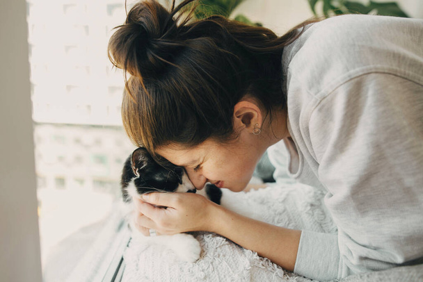 Hipster menina abraçando gato bonito, sentados juntos em casa durante quarentena coronavírus. Fica em casa em segurança. Isolamento em casa para prevenir a epidemia do vírus. Jovem mulher com gato no quarto moderno
 - Foto, Imagem