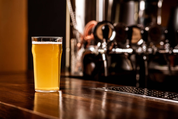 Perjantaina pubissa. Lasi kevyttä olutta puisella ruskealla baaritiskillä - Valokuva, kuva