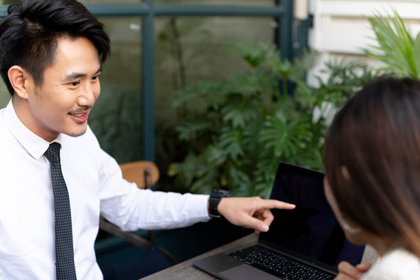 Asiático pessoas de negócios falando sobre plano de negócios, apontando o dedo para a tela do laptop fora do café
. - Foto, Imagem