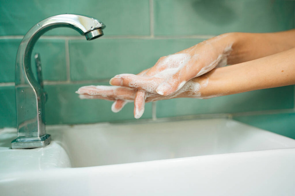 Hygiëne concept. Handen wassen met zeep onder de kraan met water in groene badkamer toilet. Wassen van handen met zeep onder stromend water. - Foto, afbeelding