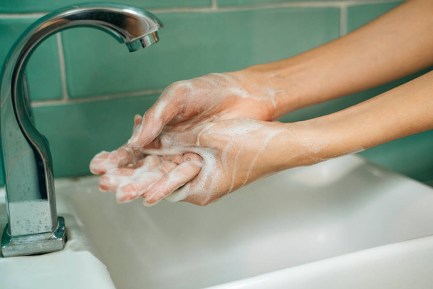 Hijyen konsepti. Musluğun altında sabunla ellerini yıkamak ve yeşil banyo tuvaletinde su içmek. Suyun altında sabunla ellerini yıkamak.. - Fotoğraf, Görsel