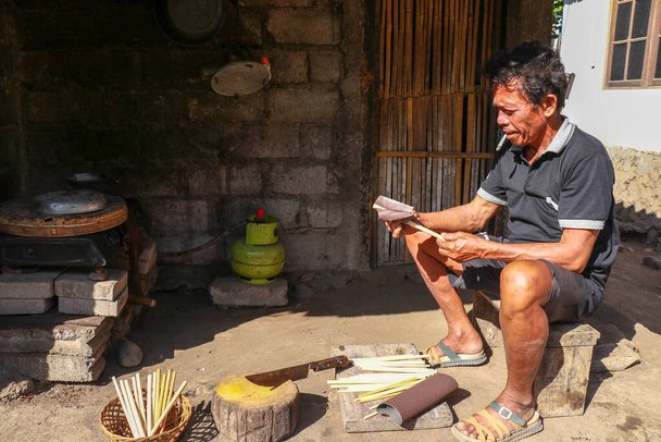 Vanha mies työskentelee bambu hänen työpaja tehdä bambu olkia, Bali, Indonesia. Ekologinen tapa tuottaa kierrätettäviä tuotteita. Etunäkymä työntekijälle, joka tekee bambupillejä - Valokuva, kuva