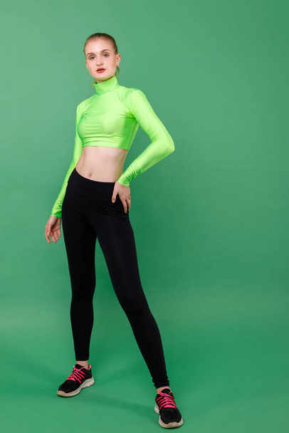 Sportief slank meisje in leggings op een groene achtergrond - Foto, afbeelding