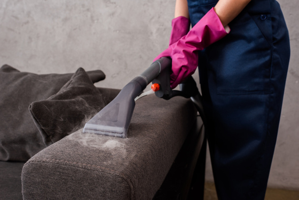 Vista cortada de limpador usando aspirador de pó com vapor quente em estofos sofá
 - Foto, Imagem