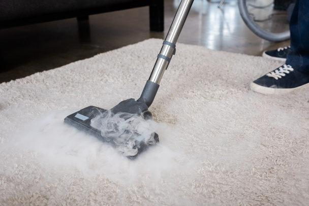 Vue recadrée du nettoyeur à l'aide d'aspirateur à vapeur chaude sur tapis à la maison - Photo, image