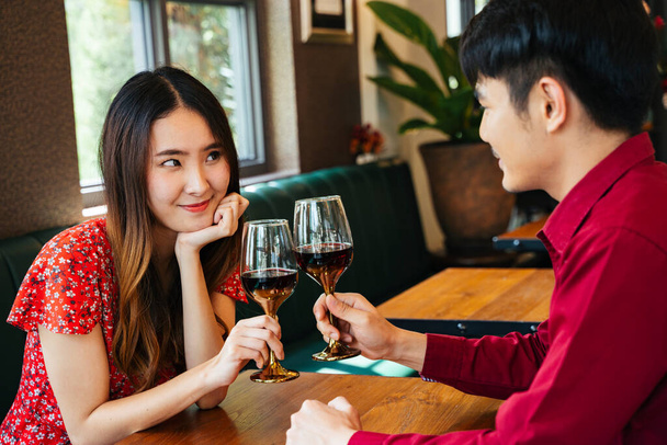 Celebrating in Valentine day. Asian couple in red dress toasting red wine glasses in restaurant. - Photo, Image