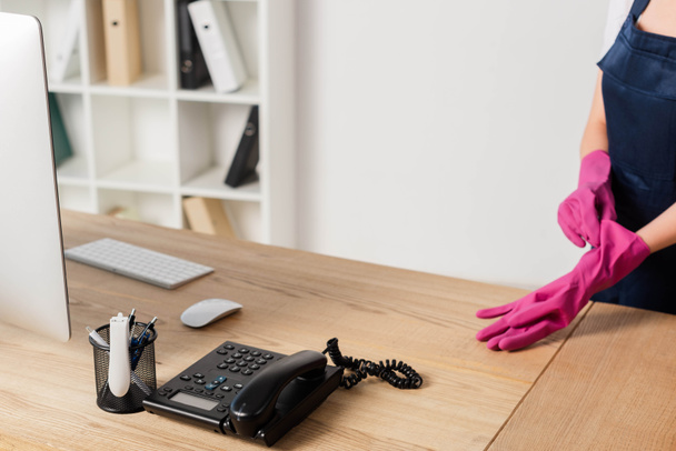 Widok na czystsze noszenie gumowej rękawiczki w pobliżu komputera i telefonu na stole biurowym   - Zdjęcie, obraz