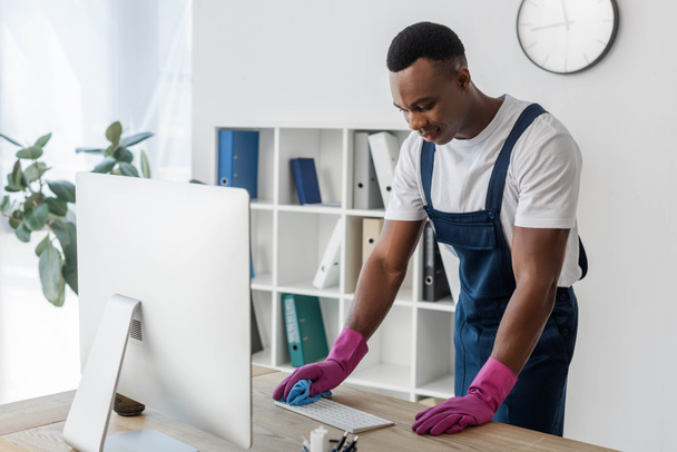 Afrikkalainen amerikkalainen työntekijä siivouspalvelu puhdistus tietokoneen näppäimistö rätti toimistossa  - Valokuva, kuva