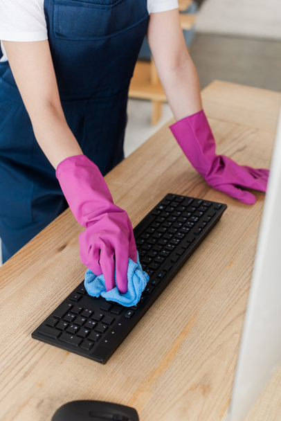 Cropped view of worker of cleaning service cleaning computer keyboard with rag on table  - Photo, Image