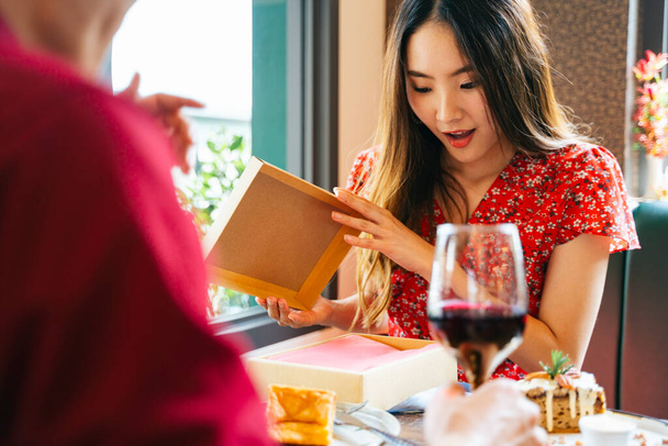 Excited surprise asian woman on red dress opening the present gift box that she got it from her boyfriend. - Φωτογραφία, εικόνα