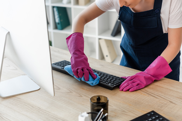 Widok przycięty czyściciela w gumowych rękawiczkach czyszczenie klawiatury komputera w biurze  - Zdjęcie, obraz