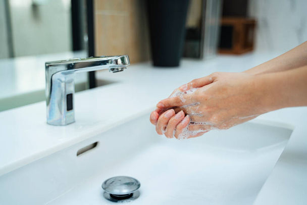 Egy nő kezet mos vízzel és szappannal a mosdóban. Kézzel nő nyitó ezüst csaptelep vagy víz csaptelep fehér mosdó nyilvános WC. - Fotó, kép