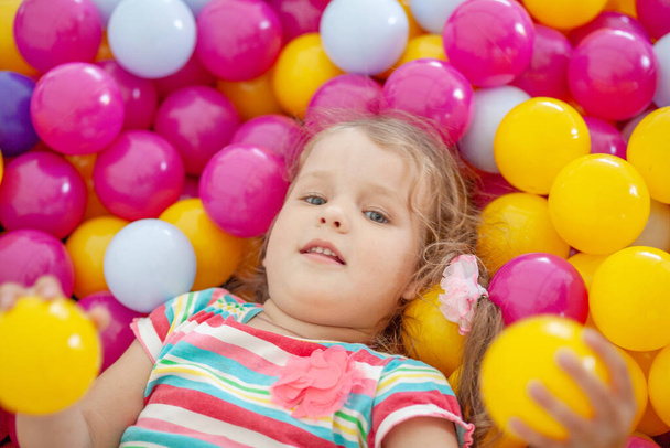 Malá roztomilá dívka hraje v jasných barevných plastových kuliček, dětský volný čas. - Fotografie, Obrázek