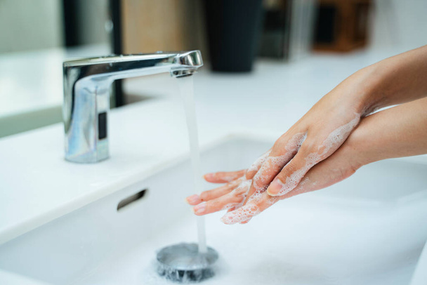 Woman washing hands with water and soap in bathroom sink. Hands woman opening silver faucet or water tap with white washing sink in public toilet. - Foto, imagen
