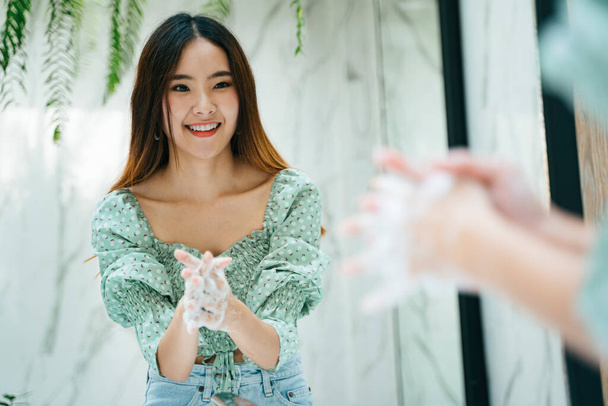 Schöne asiatische Frau auf der Mode grünes Hemd Hände waschen mit Wasser und Seifenblase im Toilettenbad. Blick in den Spiegel. - Foto, Bild
