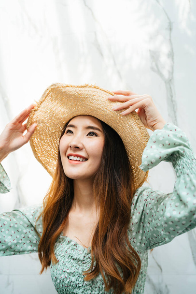 Close up portrait of beautiful young asian long hair woman wearing hat and green fashion shirt standing over granite background. - Photo, Image