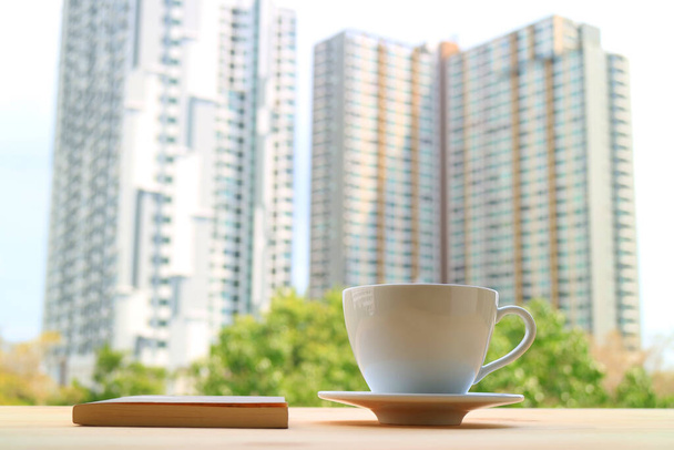 Taza de café con un libro contra edificios altos modernos borrosa en el telón de fondo
 - Foto, Imagen