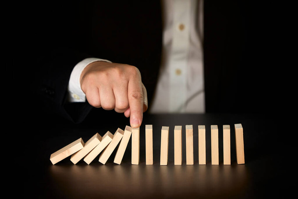 Egy üzletember keze megállítja a dominókat. Üzleti koncepció. - Fotó, kép