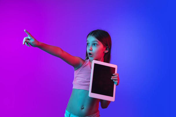 Little caucasian girls portrait isolated on gradient pink-blue background in neon light. - Фото, изображение